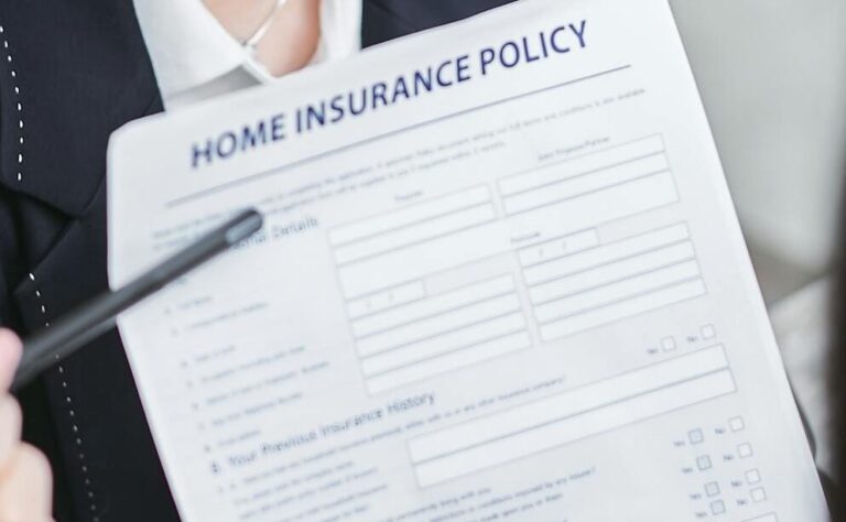 Professional woman wearing a face mask discussing a home insurance policy with a client at a desk.